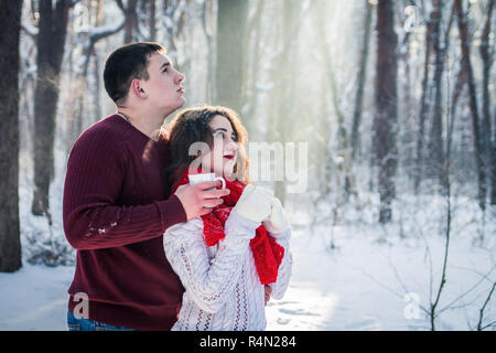 Young couple drinks tea in winter forest. Young people having picnic outdoors together Stock Photo