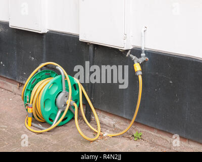 a rolled up hose plugged into the tap at the side of a house with no water running hosepipe ban uk heat save Stock Photo