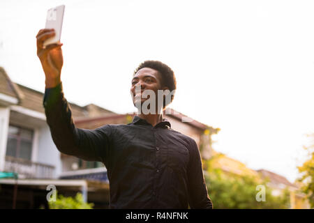 Young handsome African man using mobile phone outdoors Stock Photo