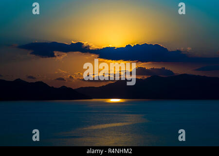 Diffused light from the setting sun filters through a band of clouds over the sea in Komodo National Park, East Nusa Tenggara, Indonesia, casting a bright patch of light onto the water. Stock Photo