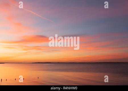 Sunset over calm water beneath thin cirrostratus with streaks of cirrus (and slight altocumulus), Seasalter, Kent, England, UK. Stock Photo