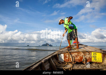 A boat captain raises the anchor on a boat along that coast of Krabi, Thailand before a ride to Railay Beach, a popular tourist destination. Stock Photo