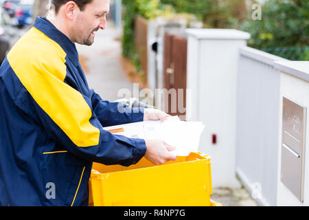 Postman delivering letters to mailbox of recipient Stock Photo