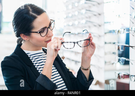 Woman taking glasses off shelf in optician shop Stock Photo