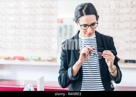 Woman taking glasses off shelf in optician shop Stock Photo