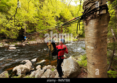 Climber traversing across the Au Sable River to access the climbing a route on Moss Cliff above Wilmington Notch, Adirondack Mountains, New York State, USA Stock Photo