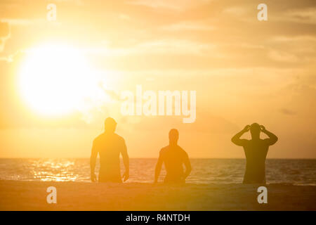 View of silhouettes of three men in swimming caps on beach at sunrise,Â PlayaÂ delÂ Carmen,Â QuintanaÂ Roo, Mexico Stock Photo