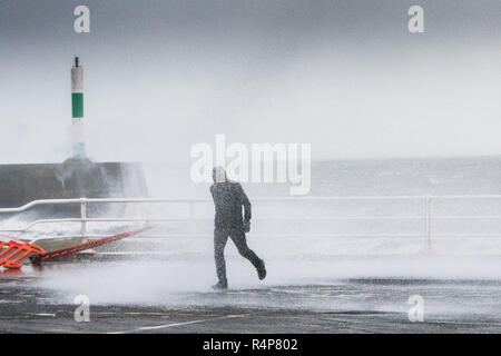 Aberystwyth Wales UK, 28th Nov 2018. UK Weather : Storm Diana, with strengthening winds gusting up to 60 or 70mph, continues to throw huge waves against the sea defences in Aberystwyth on the Cardigan Bay coast of west Wales. One foolhardy man takes a risk in getting up close to the breaking waves on the promenade.  The UK Met Office has issued a yellow warning for wind today and tomorrow for western part of the British Isles, with the risk of damage to property and likely disruption to travel.  photo credit Keith Morris / Alamy Live News Stock Photo