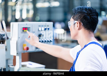 Worker pressing buttons on CNC machine in factory Stock Photo
