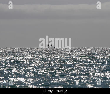 Irish fishing boat in Irish waters on the Atlantic Ocean horizon on a shimmering silvery surface of sunlit waves. Stock Photo