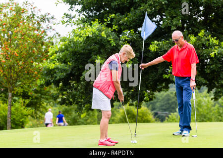 Senior woman and man playing golf putting on green Stock Photo