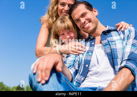 Girl on dads lap, Mom sitting next to them in field Stock Photo