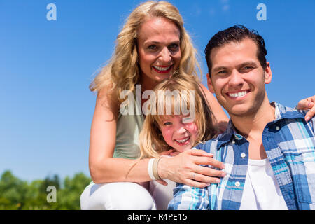 Girl on dads lap, Mom sitting next to them in field Stock Photo