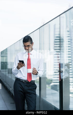 Indian businessman drinking coffee and using a smartphone Stock Photo