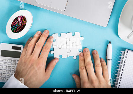 Businessperson Joining Puzzle On Desk Stock Photo