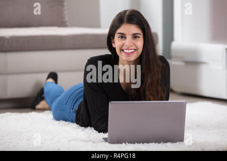 Young Woman Lying On Rug Using Laptop Stock Photo