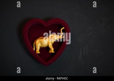 A gold elephant figurine inside a heart-shaped box. Stock Photo