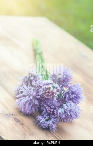 Flower chives tied in a snop on a natural wooden cutting board Stock Photo