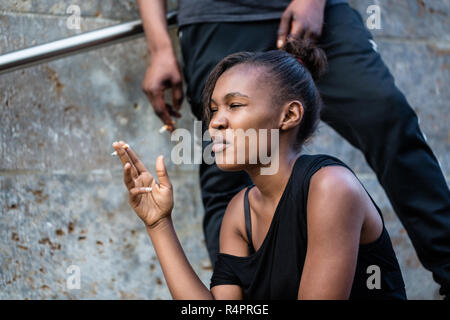 Young African American woman and man smoking outdoors in the city Stock Photo