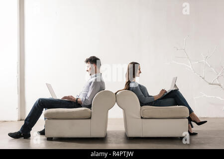 Man and woman sitting back-to-back in empty room working on laptops Stock Photo