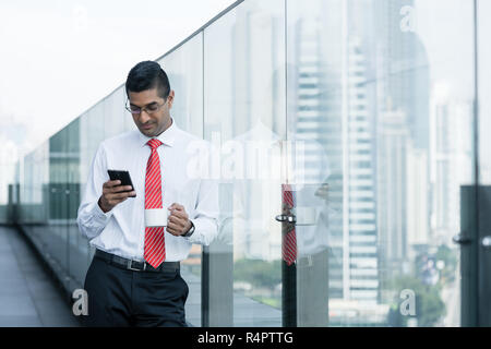 Indian businessman drinking coffee and using a smartphone Stock Photo