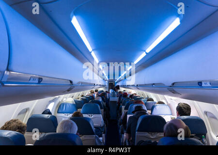 Interior of airplane full of seated passengers while in flight with EXIT sign clearly visible Stock Photo