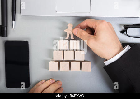 Businessperson Arranging Human Figure Cut Out On Wooden Blocks Stock Photo