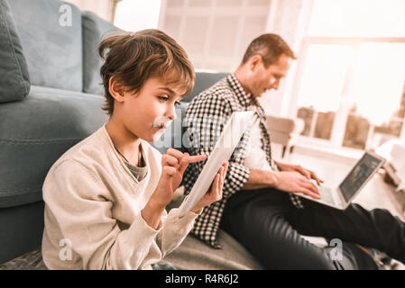Father working on his laptop and his son playing on his tablet. Stock Photo