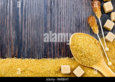 Sugar brown granules in a spoon, cubes and crystals on a stick in the form of a frame on the background of a wooden board Stock Photo