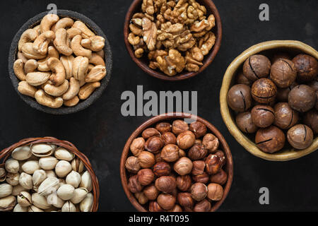 Various nuts in bowls on black background. Hazelnut, cashew nuts, pistachios, macadamia and walnuts. Top view Stock Photo