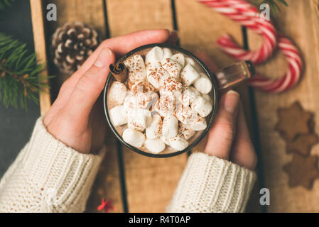Cup of hot chocolate with marshmallows in girl hands. Female holding warm cozy comfort drink. Top view, toned image Stock Photo