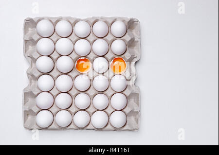 Eggs in paper tray with two  cracked open with yellow yolk .Careful storage of edible eggs.  The egg diet concept. Stock Photo