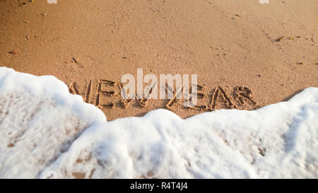 Closeup image of sea waves rolling over words New Year written on wet sand on the beach. Concept of winter holidays, Christmas and tourism Stock Photo