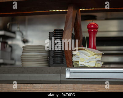 Receipts stacked up with serving bowls and plates sitting on a restaurant kitchen counter