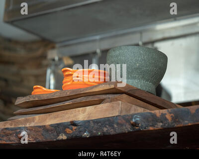 Orange bowls and gray mortar and pestle sitting on a wooden restaurant serving counter Stock Photo