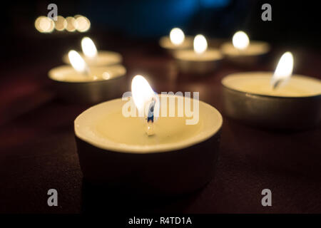 Tealight candles burning the flames dimly illuminating the area. Stock Photo