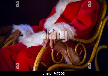 Santa Claus having a rest in a comfortable chair near the fireplace at home. Stock Photo