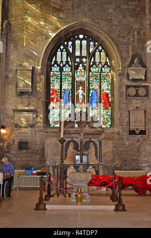 An ornate stained glass window within the Church of St John the Baptist in the market square of Cirencester with a stone font in the foreground. Stock Photo