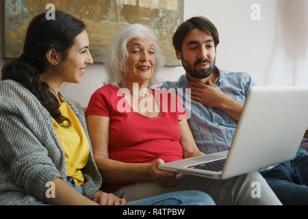 Senior mother using laptop with daughter and son on living room sofa Stock Photo