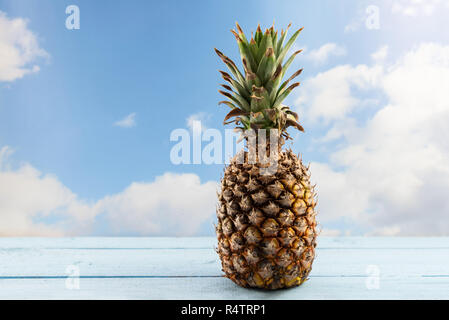 organic pineapple fruit on a wooden table against a blue sky with clouds, copy space Stock Photo