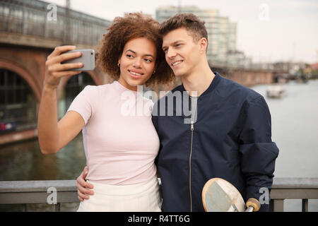 Young couple with smart phone taking selfie on bridge Stock Photo