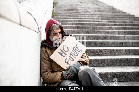 Homeless beggar man sitting on stairs outdoors in city holding no future cardboard sign. Stock Photo