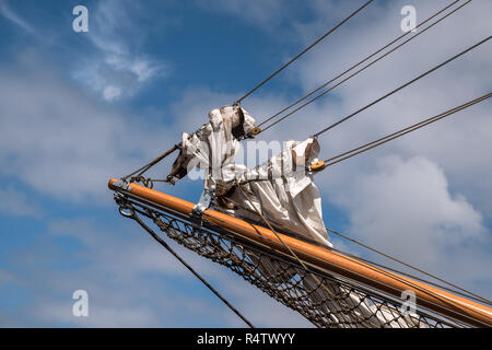 jib boom with reefed sails on the bow of a historic sailing ship against a blue sky with clouds, copy space Stock Photo