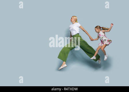 Mother and daughter jumping against blue background Stock Photo