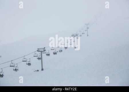 Skiers riding ski resort chair lift up mountainside Stock Photo