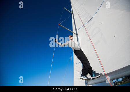 Low angle view of smiling man standing on yacht boom Stock Photo