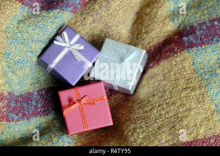 Three holiday gifts in small colored boxes, covered with ribbon with bows, against a background of woolen fabric top view close-up Stock Photo