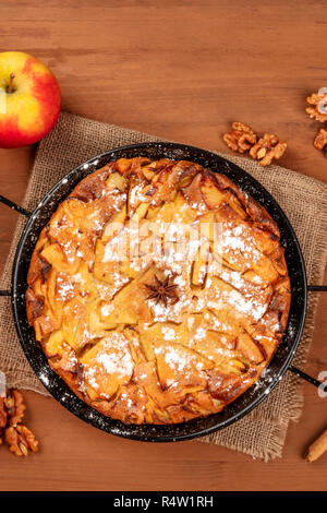 A closeup photo of an apple pie, shot from the top on a dark rustic wooden background with an apple, walnuts, anise, and a place for text Stock Photo