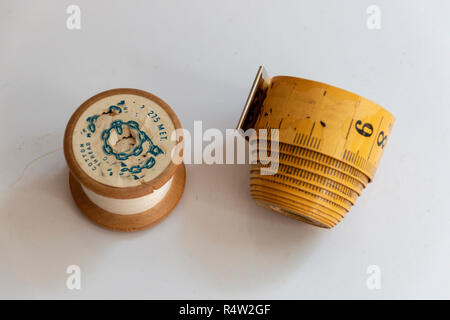 A close up view of a old wooden cotton bobben reel and an old measuring tape that has faded on a isolated white background Stock Photo