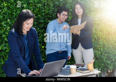 Asian business woman using computer laptop and her team dicussing something while working. Stock Photo